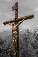 copper sculpture of the crucifixion of Christ with the trees and mountains on background