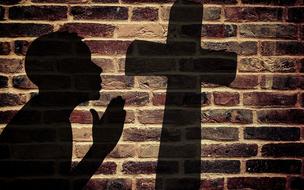 silhouette of a person, praying near the cross, at background with brick wall