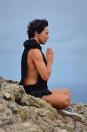 man meditates sitting on a rock