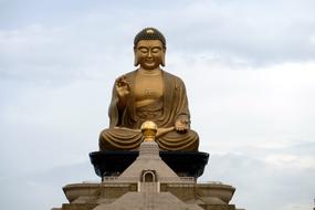 Beautiful golden statue of Buddha, on the temple in Taiwan, at cloudy sky on background