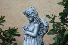 Beautiful girl angel statue with flowers among the green leaves