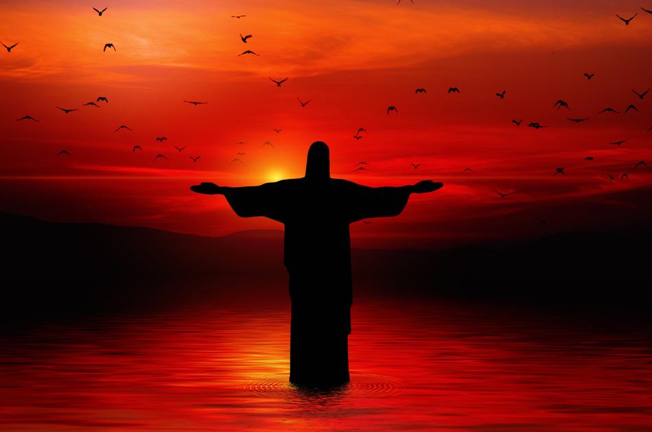 statue of Jesus Christ and a flock of birds on the background of the red sky
