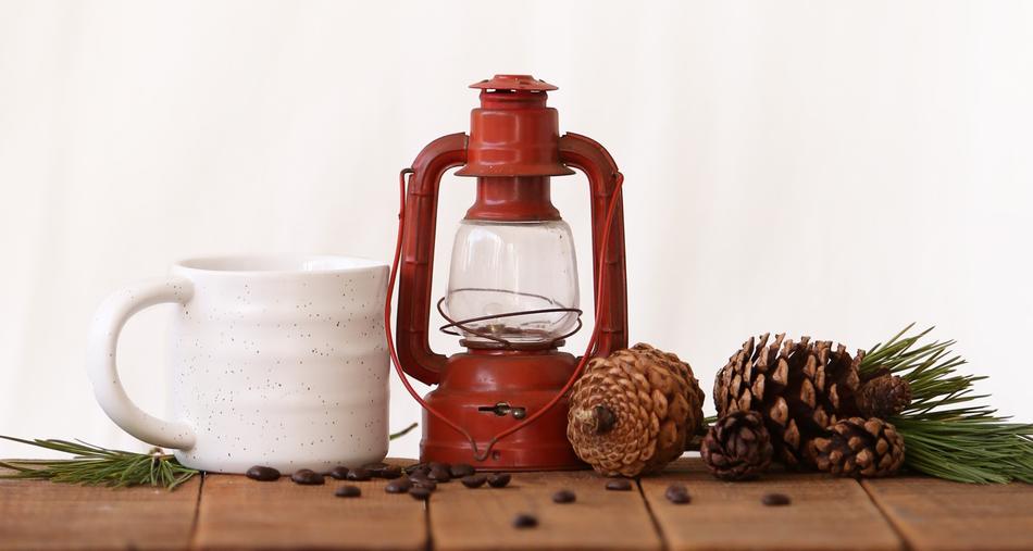 white cup, kerosene lamp and cones on the table