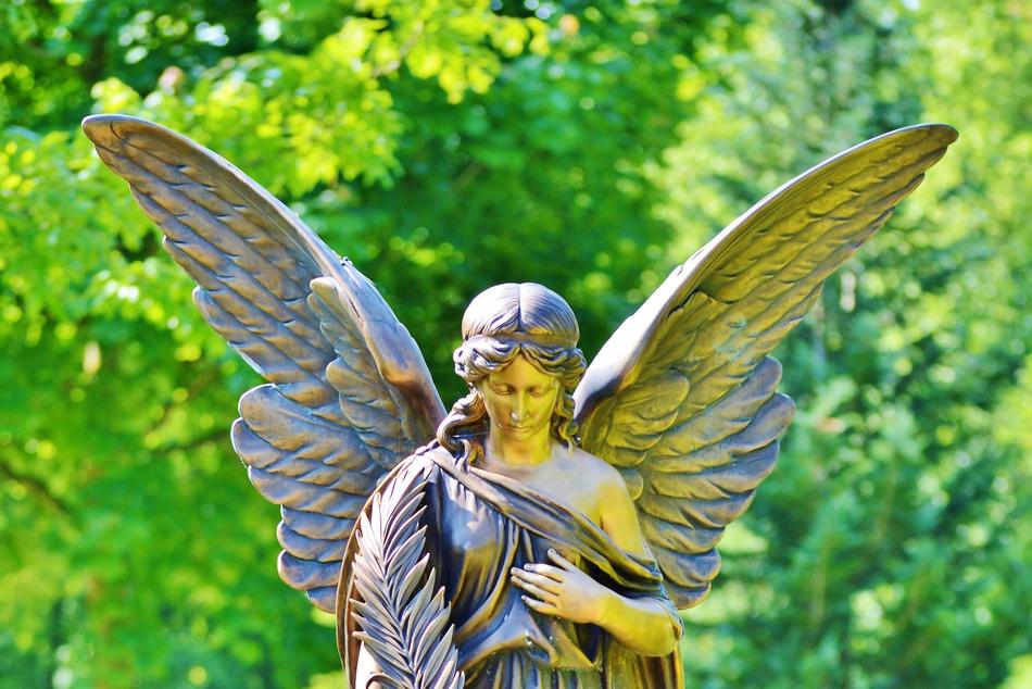Beautiful and colorful stone sculpture of the angel, near the colorful and beautiful plants, in light