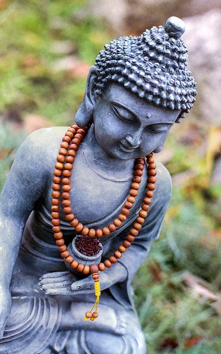 Beautiful statue of Buddha in meditation, with the praying beads, near the colorful plants