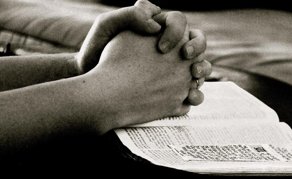 Black and white photo of the praying hands on the bible
