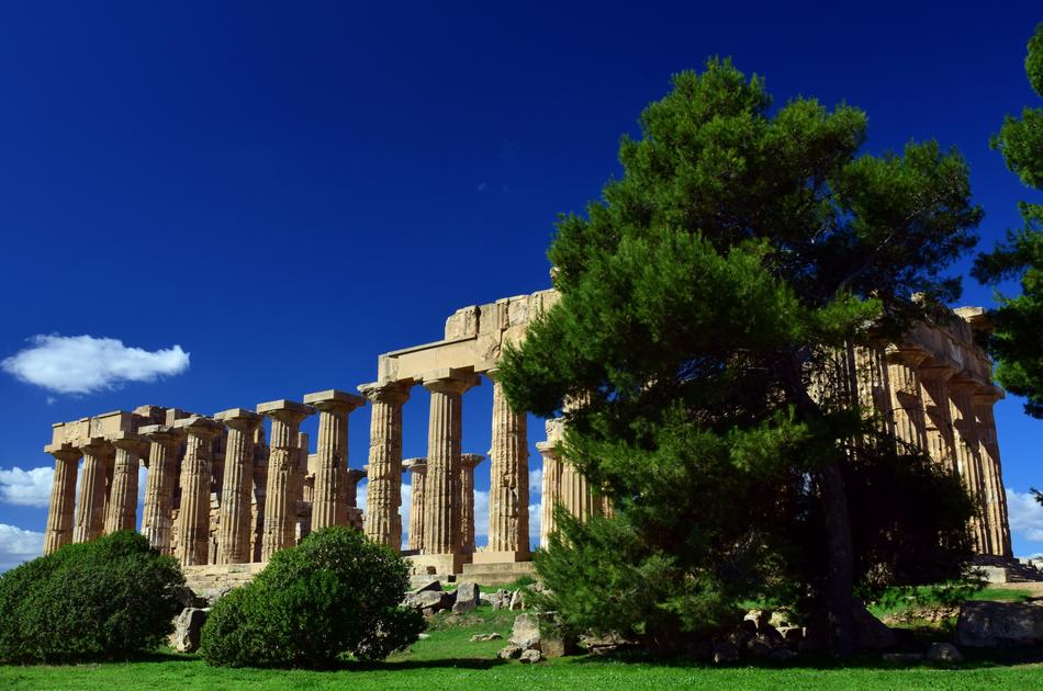 Beautiful Greek ruins among the plants at blue sky background with white clouds
