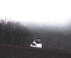 Black and white photo with the beautiful church, near the trees in fog