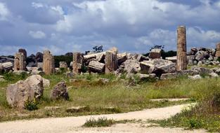 Beautiful, old ruins of the columnar temple, on the colorful field, under the cloudy sky, in Sicily, Italy