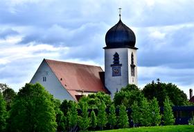 Beautiful church with the steeple with the cross, among the green trees, near the green meadow