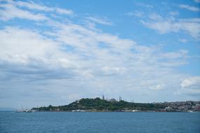 Beautiful, green shore with the mosque, among the water, at blue sky with white clouds on background, in Ä°stanbul, Turkey
