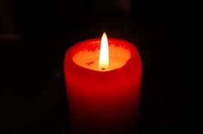 Close-up of the glowing, red and orange candle, at black background