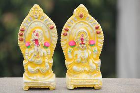 two yellow figurines depicting god lakshmi