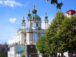 Beautiful and colorful St Andrews Church, near the colorful trees, in Kiev, Ukraine, under the blue sky with white clouds