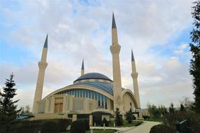 Beautiful and colorful mosque, with the minarets, among the trees, on the landscape, under the blue sky with clouds