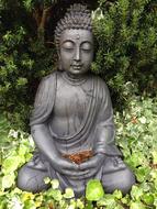 Beautiful, grey Buddha statue among the colorful plants in the garden