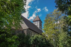 Beautiful village church with the steeple, among the colorful trees, at blue sky with white clouds on background, in Berlin, Germany