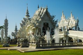 Beautiful White Temple, among the green field in Chiang Rai, Thailand, under the blue sky