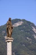 Beautiful sculpture on the column, near the green mountain, at blue sky on background