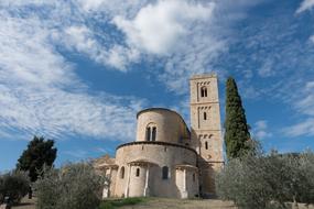 Beautiful Sant' Antimo abbey, among the green trees in Montalcino, Italy, under the blue sky with white clouds