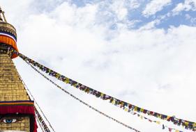 Beautiful stupa decorated with colorful prayer flags at blue sky with white clouds on background