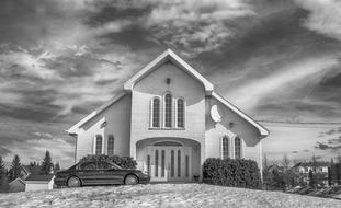 Black and white photo of the beautiful Canadian church, with the car and plants, under the cloudy sky