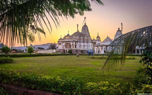 Beautiful, decorated Manas Mandir temple, among the colorful plants, at colorful sunset in Shahapur, India