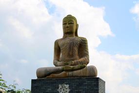 Beautiful stone Buddha sculpture, near the tree, at blue sky with white clouds on background