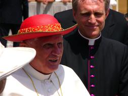 Smiling Pope Benedict in hat, among the other people in Vatican