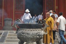 Buddhist monk in robe, near the cauldron, near the people, near the beautiful and colorful temple