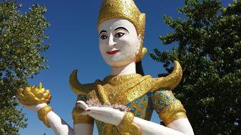 Beautiful and colorful, shiny Buddhist statue in the Cambodian Temple, among the green trees, under the blue sky