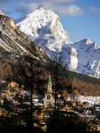 Beautiful landscape of the mountains with church and houses, among the plants, and snow, in sunlight