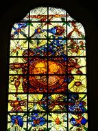 Beautiful and colorful, patterned, shiny stained glass window in the church, among the darkness