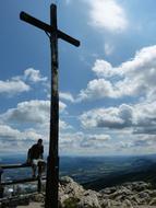 Person sitting on the bench, near the cross, on the beautiful and colorful landscape in sunlight