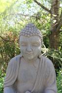 Beautiful, Eastern Buddha statue, among the green plants in sunlight