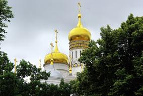 Beautiful cathedral with shiny domes, among the green trees, in Yaroslavl, Russia, under the clouds