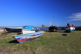 Colorful fishing boats on the green grass on the Holy Island, under the blue sky with clouds