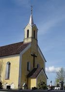 Beautiful landscape with the church with cross, among the plants, under the blue sky with clouds