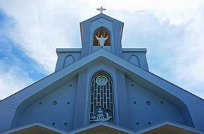 facade of a christian church with a cross on a background of clouds