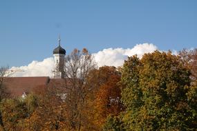 church tower with a spire behind the trees in autumn