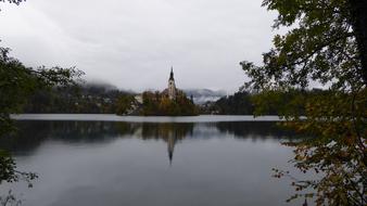 Beautiful landscape of the Lake Bled, with the shore with colorful plants and church, under the clouds, in Slovenia