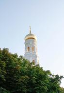 Beautiful, shiny, gold and white belfry of the church with the cross, near the colorful tree