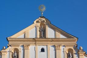 Facade of the white and beige building with the statue, in sunlight, under the blue sky