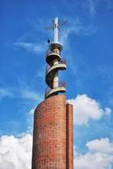 Close-up of the colorful church tower with the cross in sunlight, under the blue sky with white clouds