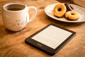 cup of tea, donuts on a plate and an e-book on the table