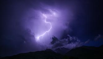 Beautiful, bright, violet lightning in the dark, cloudy sky, above the landscape