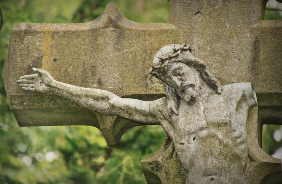 Beautiful Jesus Christ statue on the cross, near the green and yellow plants