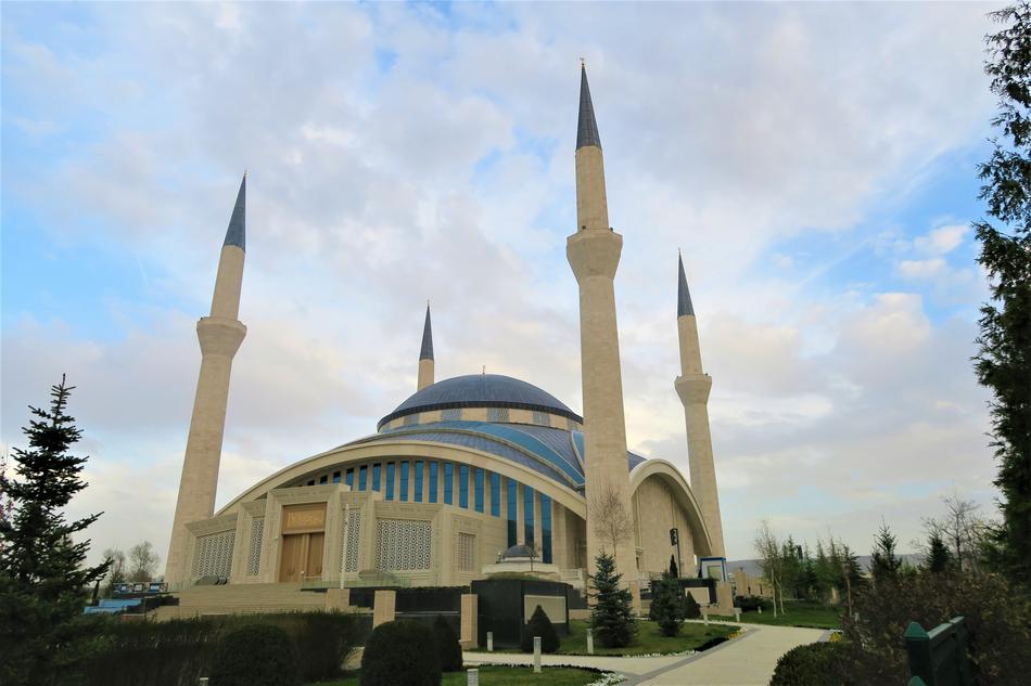 Beautiful and colorful mosque, with the minarets, among the trees, on the landscape, under the blue sky with clouds