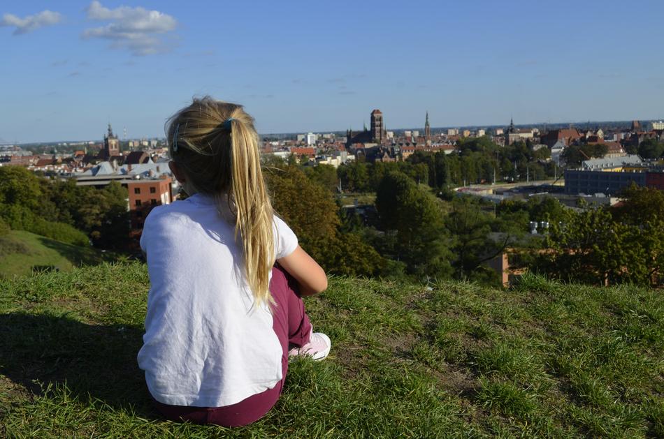 child girl sits on hill in view of city, poland, GdaÅsk
