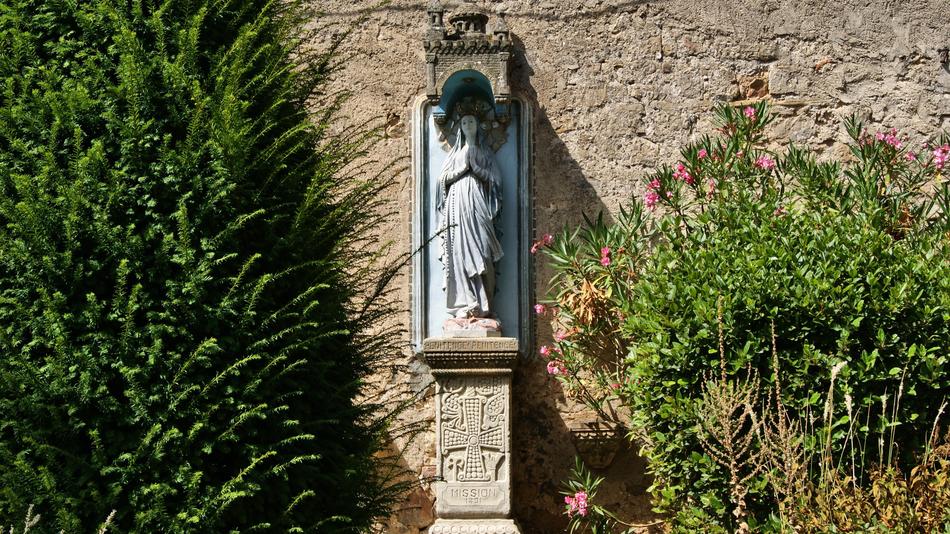 sculpture of the virgin mary near the building and green bushes